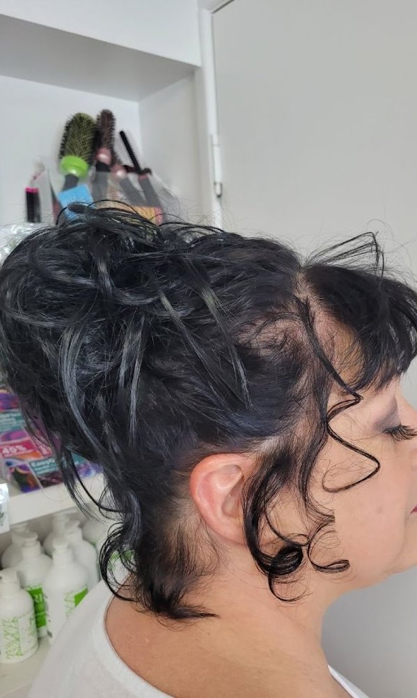 Dark curly hair piled into a textured top knot with face-framing tendrils